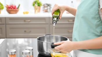 Woman pours olive oil into pot