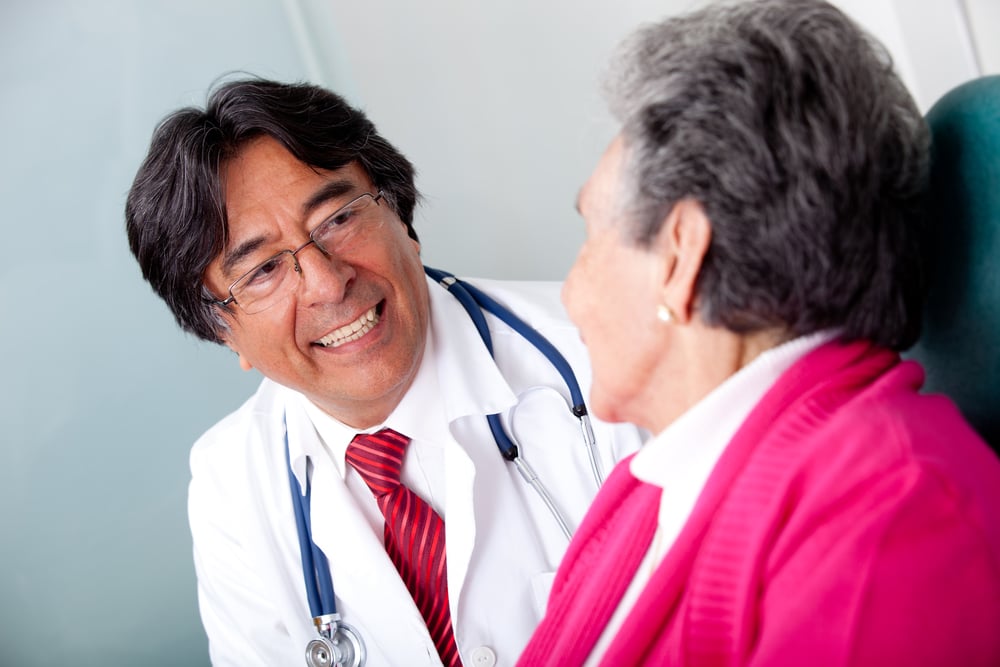 A doctor in a while lab coat with stethescope around his neck discusses anti-amyloid drugs to slow progression of Alzheimer's with a female patient in her early 70s.