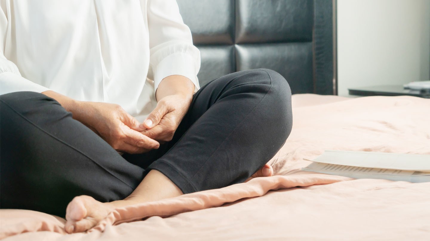 Woman sits with crossed legs and hands folded in lap