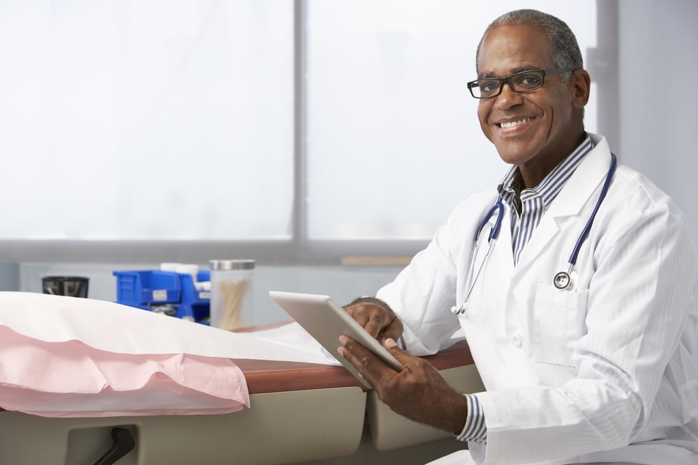 primary care doctor holds iPad and smiles for camera